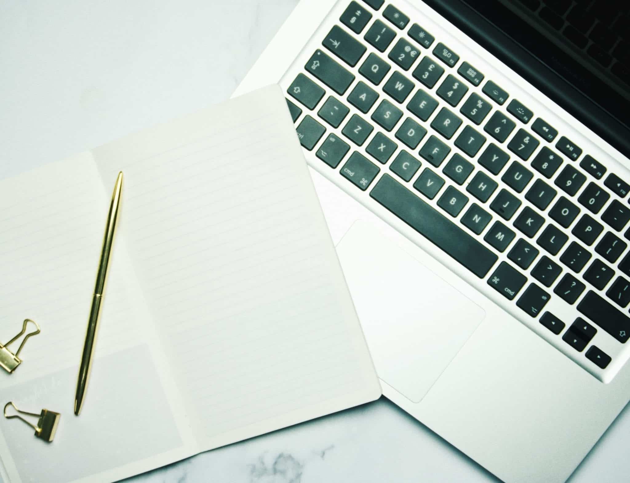 Notebook with a golden pen on top of a laptop keyboard.